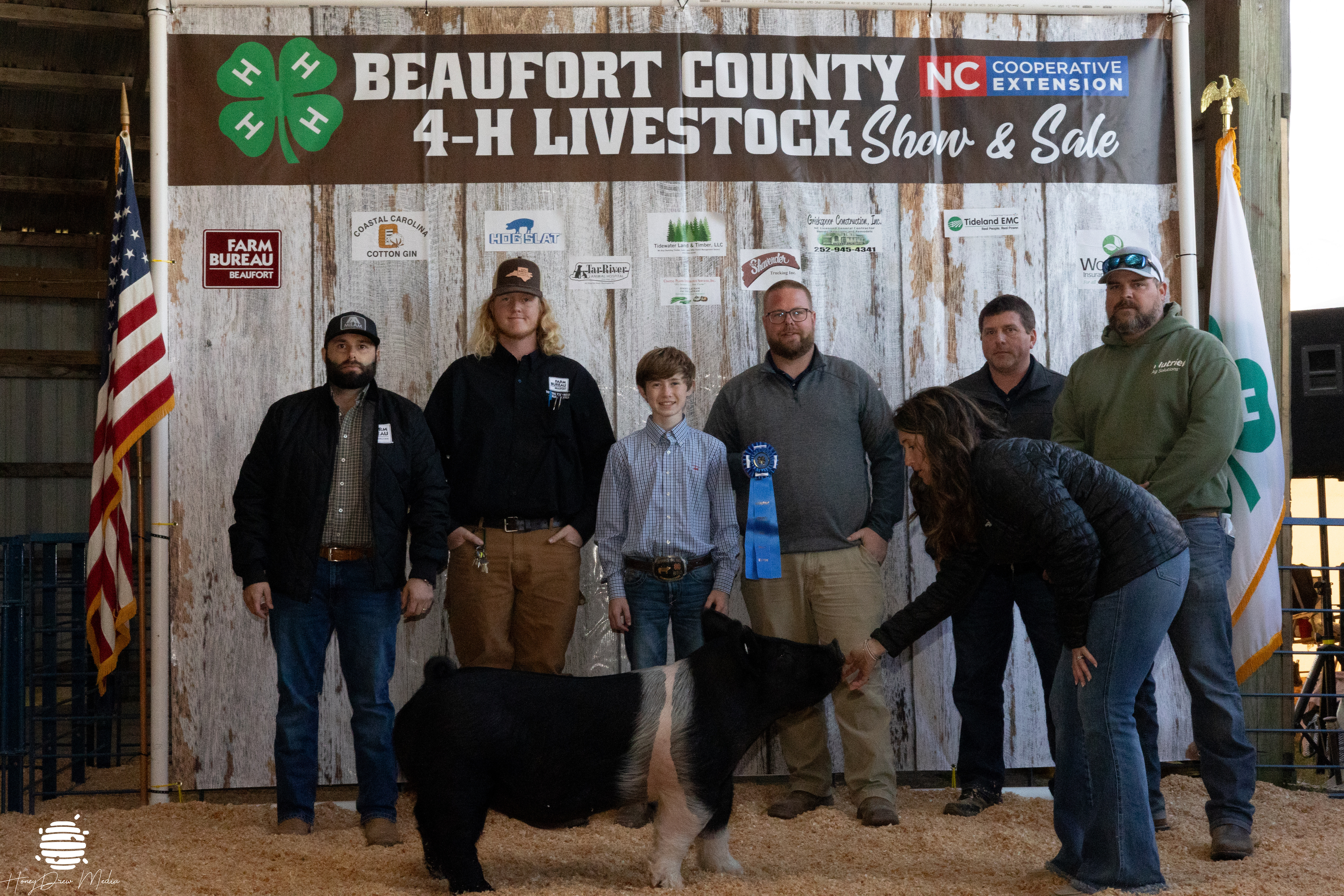 Picture of Dylan Briley with his hog and the buyers of his animal in front of the 4-H Livestock Show banner.