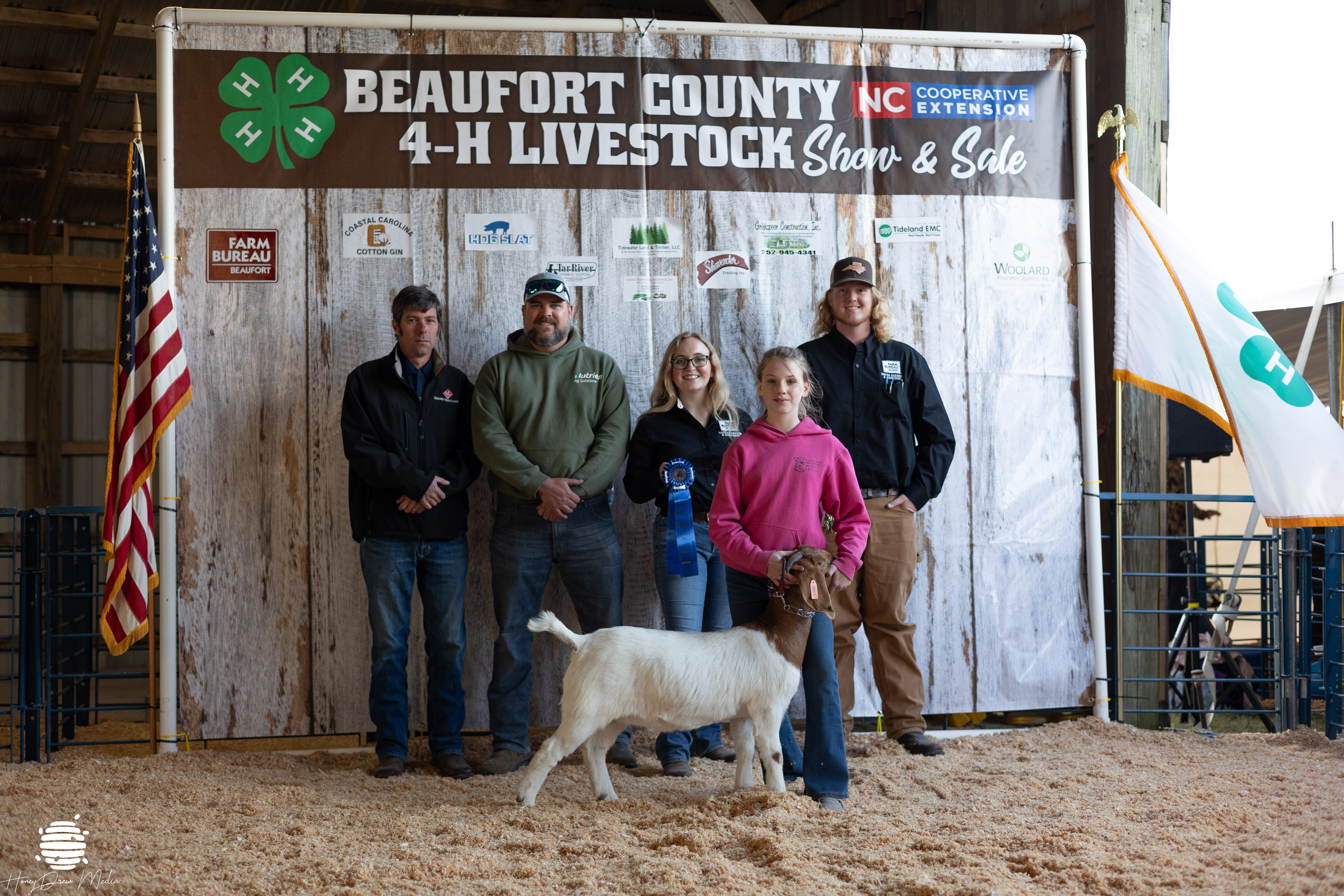 A group of kids and adults posing with a ribbon and a goat.