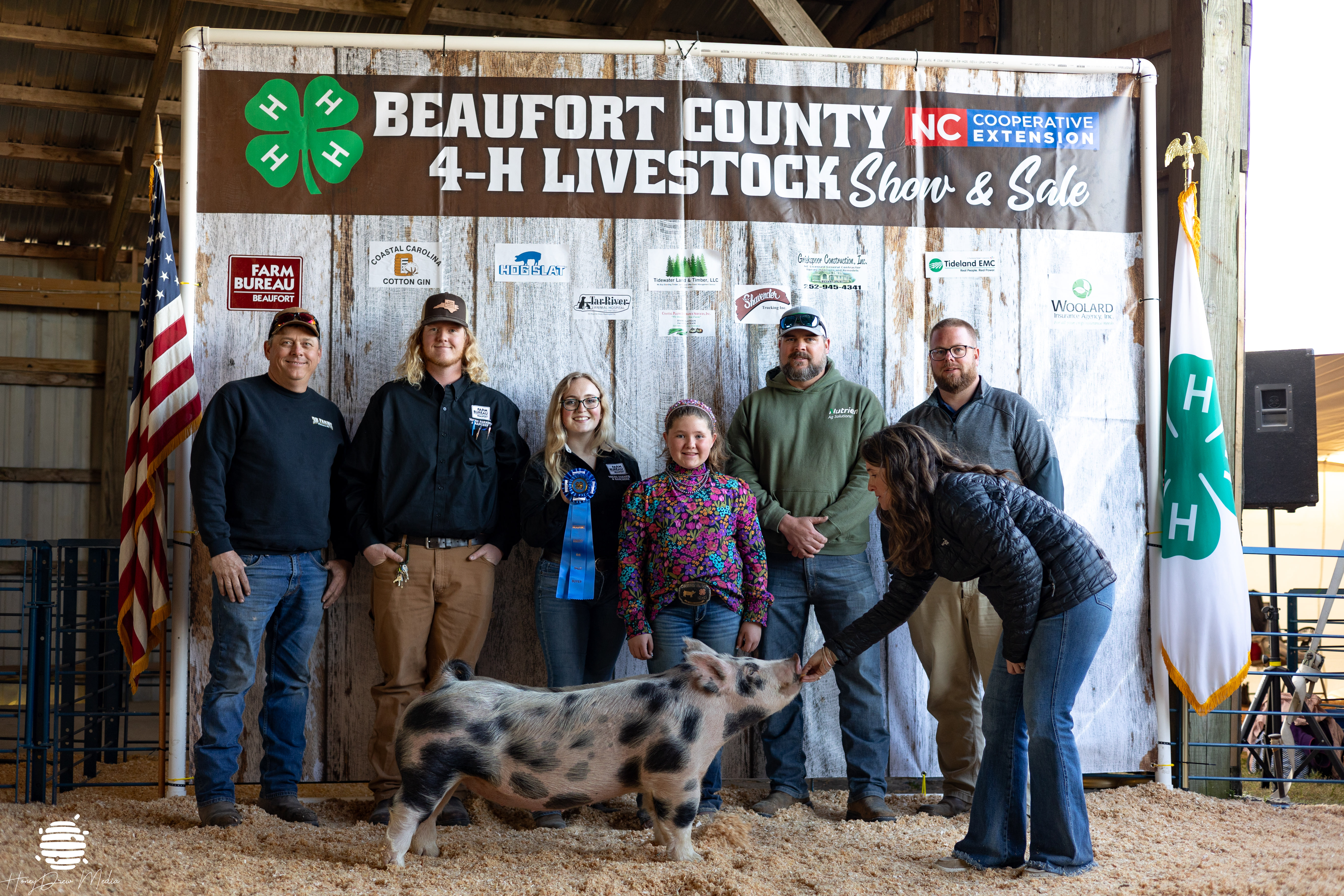 A group of kids and adults posing with a ribbon and a pig.