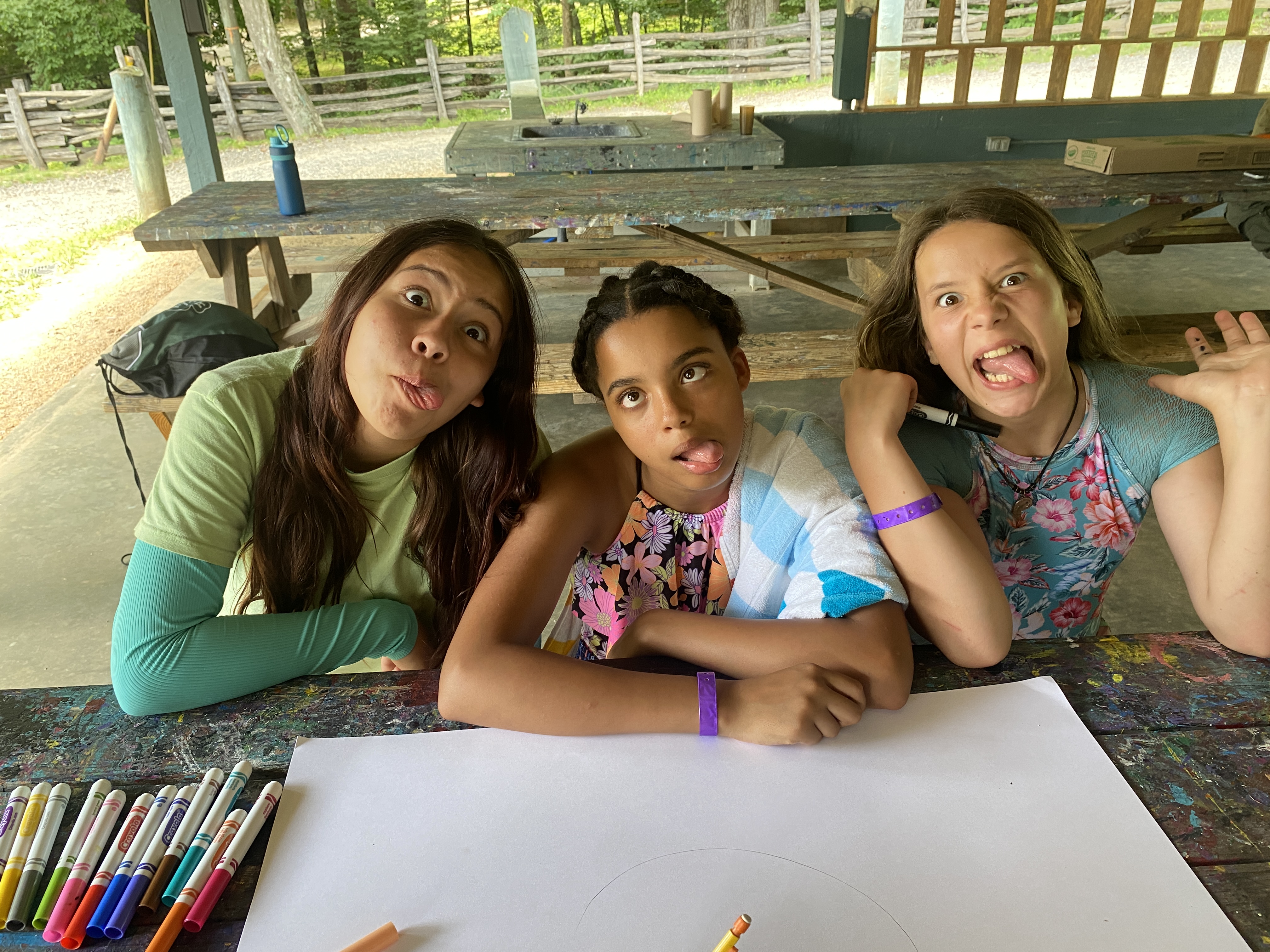 Three youth sitting at a picnic table making silly faces.